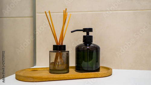A bottle of liquid soap and scented sticks on a wooden stand.