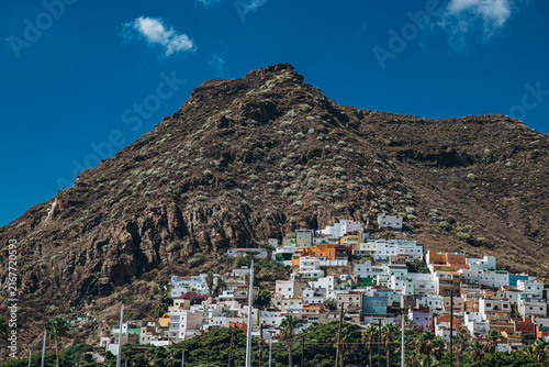 фотографія Colorful hillside village with rugged mountain backdrop on a sunny day