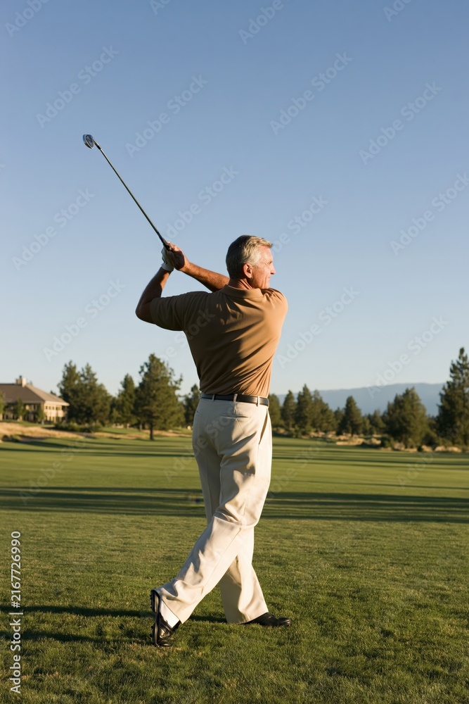 Obraz premium Mature man finishing golf swing on a manicured course with long shadow for banner and background design