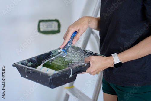 Person loads roller with green paint in tray before painting interior wall