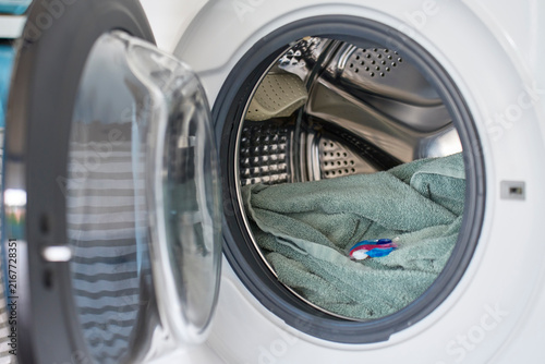 Open washing machine with towel and detergent capsule inside drum