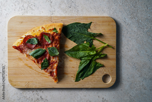 Pepperoni pizza slice with spinach on cutting board