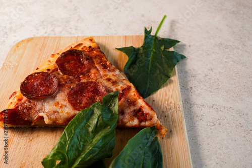 Pepperoni pizza slice on wooden board with basil