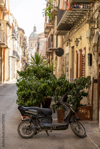 Parked scooter on a narrow historic street surrounded by traditional italian architecture and urban greenery