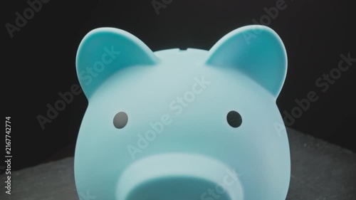 Man putting coins into piggy bank against black background. Saving money for future use. Piggy bank as a concept for storing, accumulating, and saving financial resources. Close-up in 4K, UHD