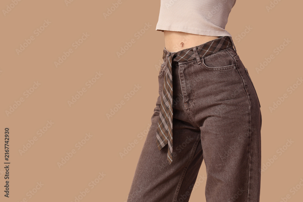 Obraz premium Young woman in stylish brown jeans on beige background, closeup
