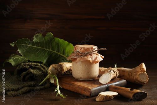 Cuadro en lienzo Jar with horseradish sauce, roots and leaf on wooden background
