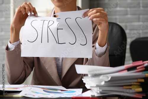 Young businesswoman holding paper with word STRESS and documents on table in ...