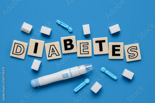 Foto Word DIABETES with lancet pen, sugar and disposable needles on blue background