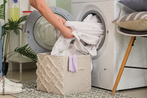 Woman taking white clothes from washing machine in laundry room