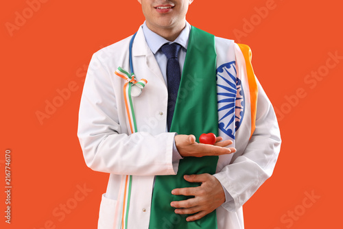 Male physician with flag of India, ribbon and heart on orange background, clo...