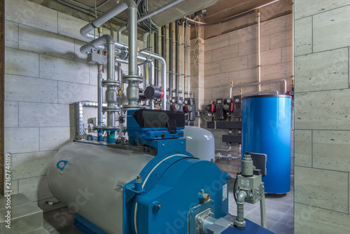 The boiler and piping system are set up in a mechanical room within a commercial building. Pipes connect to various equipment and meters. The setting is typical for such facilities