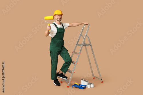 Portrait of male painter with paint roller and stepladder on beige background