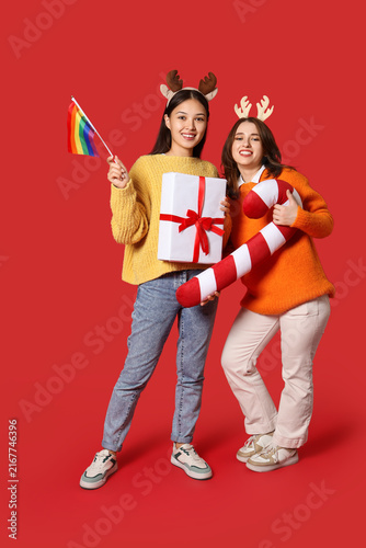Young lesbian couple with LGBT flag, Christmas gift and candy cane pillow on ...