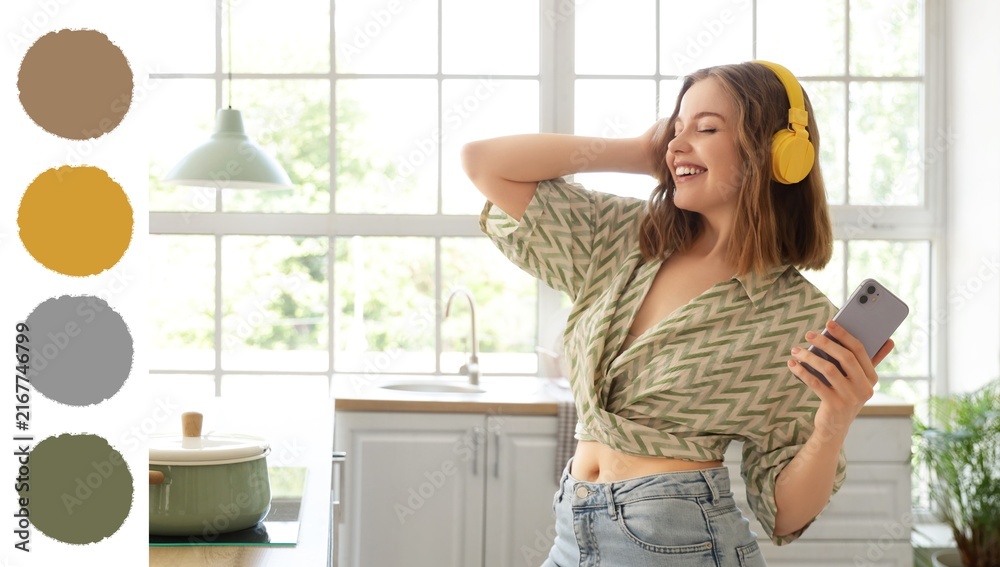 Fototapeta premium Joyful home entertainment and relaxation, young woman dancing with headphones and smartphone in a modern kitchen