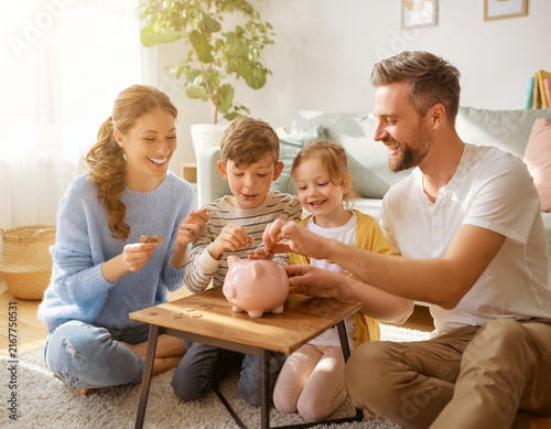 A joyful family saving money together with a piggy bank in a bright living room.