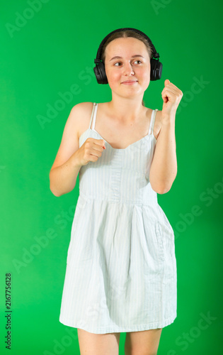 Obraz na płótnie Young teenage girl stands against green screen in summer dress, listening to mus