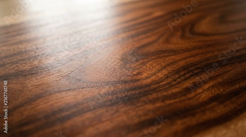 Rich mahogany wood surface close-up showing deep brown and reddish flowing grain patterns with smooth polished texture and warm natural tones for furniture and design backgrounds