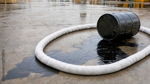 Oil spill response in industrial area with a black barrel and absorbent boom