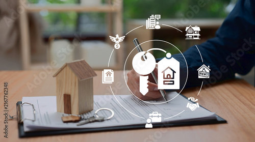 Real estate agent signing contract with miniature wooden house and keys on desk