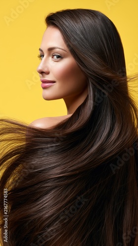 Attractive woman with long flowing brown hair smiling confidently with smooth glowing skin against bright yellow background for beauty concept