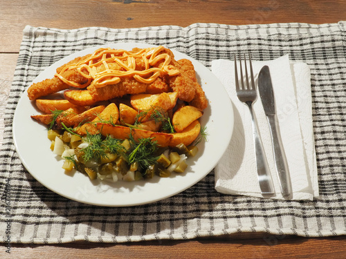 Obraz na płótnie Golden brown fried chicken tenders sit beside crispy potato wedges on a white plate
