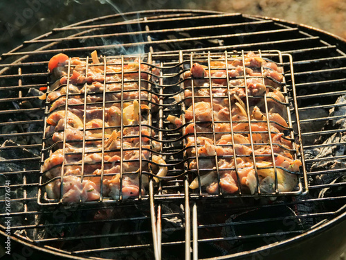Canvastavla Two metal grills hold skewered chicken pieces over smoky charcoal