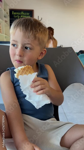 Little boy eating delicious ice cream in waffle cone at cafe
