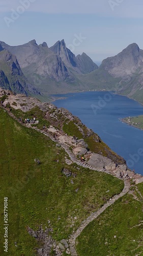 Aerial view of people hiking along stone steps on Reinebringen mountain ridge above Reinefjorden in Lofoten Islands Norway during a sunny day.