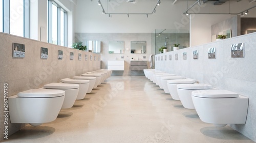 row of modern white wall mounted toilets in bathroom equipment showroom store