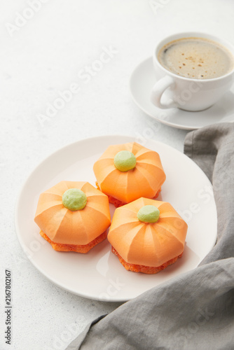 Pumpkin shaped desserts on a white plate, with a cup of coffee and gray napkin on the side