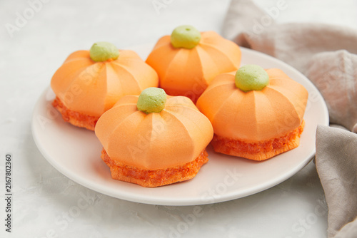 Four orange pumpkin shaped desserts with green tops, displayed on a white plate with a gray napkin