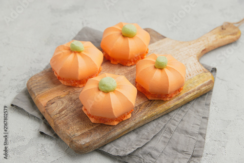 Four pumpkin shaped desserts with green tops on a rustic wooden board with a gray napkin