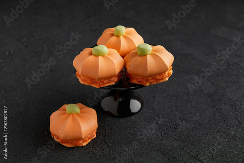 Four pumpkin shaped meringue desserts with green tops placed on a black stand in a dark setting