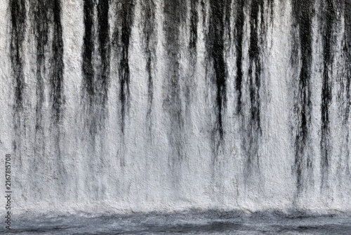 Water cascading in a powerful waterfall creating vertical streams and dynamic flow against a natural backdrop in grayscale tones