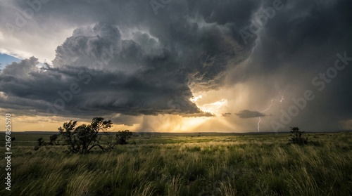 Dramatic Thunderstorm Over Open Prairie Plains with Lightning Strike and Sun Rays
