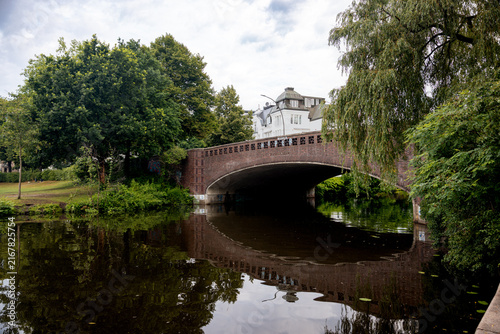 Arched stone bridge crossing an Alster waterway surrounded by lush summer vegetation in Hamburg, Germany.