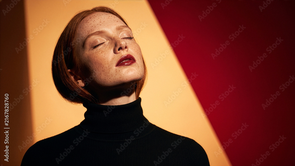 Obraz premium Young Woman With Freckles And Red Lipstick Enjoys Sunlight With Eyes Closed