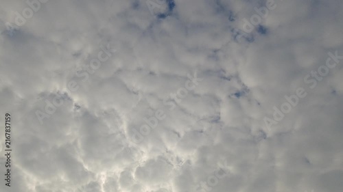 Dense white and grey clouds moving slowly across a bright sky. Beautiful overcast skyscape with soft natural lighting and small patches of blue. Perfect for weather and atmospheric backgrounds.
