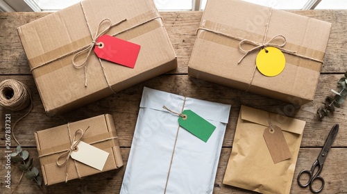 Overhead view of various packages and envelopes tied with twine and adorned with colorful tags on a rustic wooden table