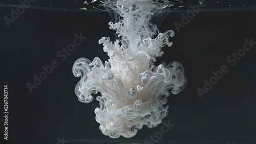White ink swirls gracefully underwater against a deep black backdrop.