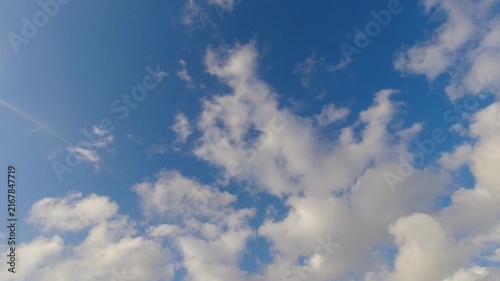 Beautiful bright blue sky with fluffy white clouds moving gently. A small flock of birds flies past the peaceful sunny background. Perfect for freedom and nature concepts.