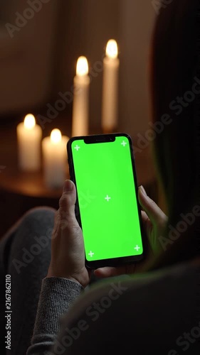 Woman Holding a Smartphone with Green Screen Chroma Key Display in a Cozy Candlelit Room at Night