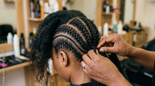 Professional hairstylist braiding hair of a young woman in salon