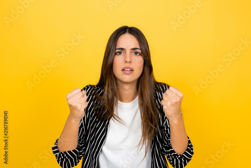 Fotografía Young frustrated woman standing on a yellow background, raising and clenching he
