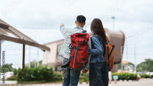 Rear view of Asian couple backpackers pointing at destination during outdoor travel
