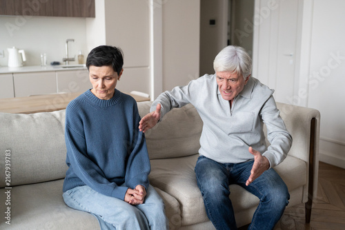 Bild auf Leinwand Elderly couple in conflict, man blaming woman while frail female fears speaking due to abusive dynamic