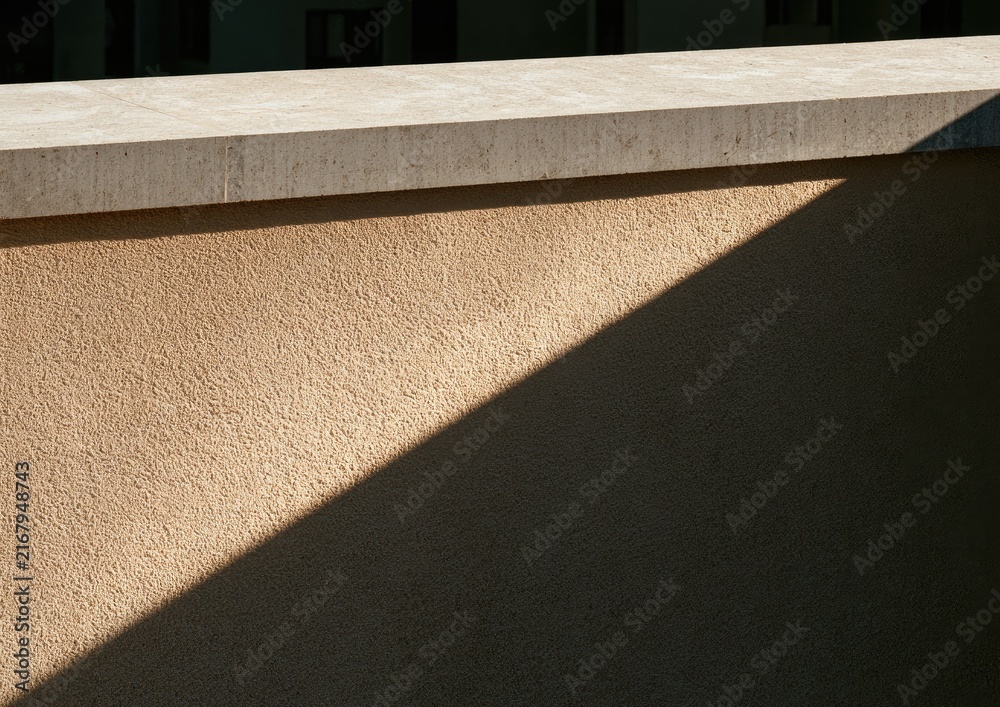Fototapeta premium Sunlit textured wall with a sharp shadow and stone trim