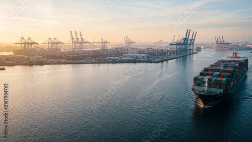 Large Container Ship Navigating Port Terminal Harbor with Gantry Cranes at Golden Hour