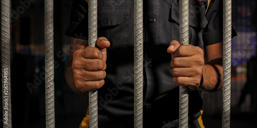 Fotografie prisoner's hands behind bars with black background